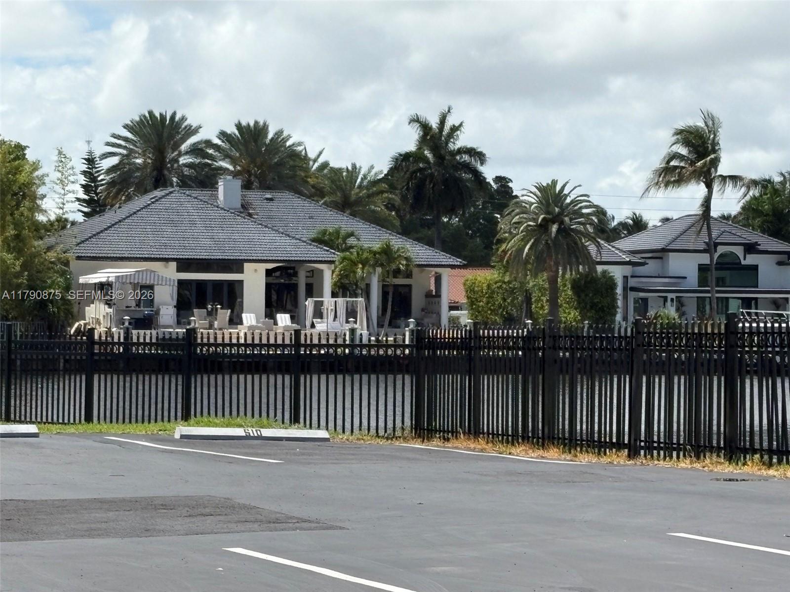A black metal fence separates a parking lot from a waterfront house with palm trees — 701 Three Islands Blvd # 409, Hallandale Beach FL 33009, HALLANDALE BEACH, FL