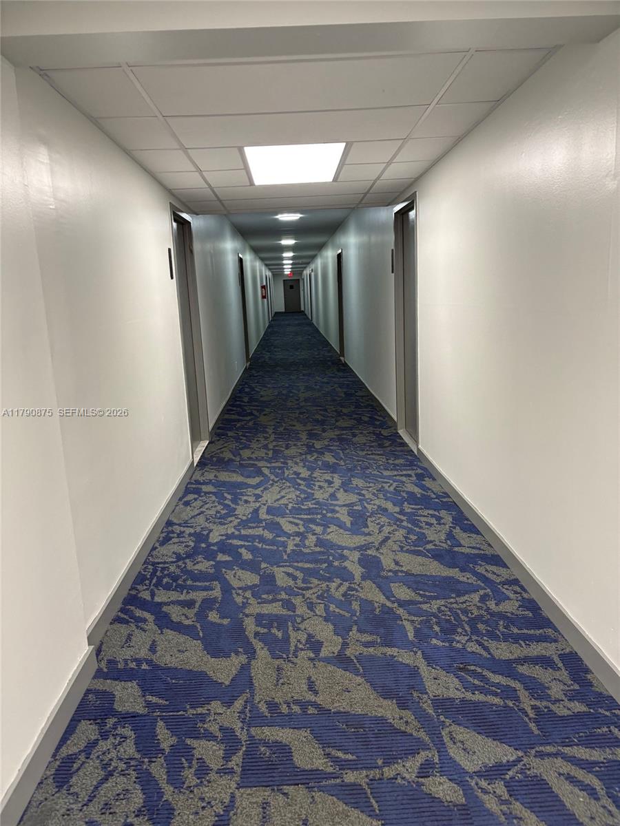 A long, narrow apartment hallway features white walls, a blue patterned carpet, and recessed lighting — 701 Three Islands Blvd # 409, Hallandale Beach FL 33009, HALLANDALE BEACH, FL