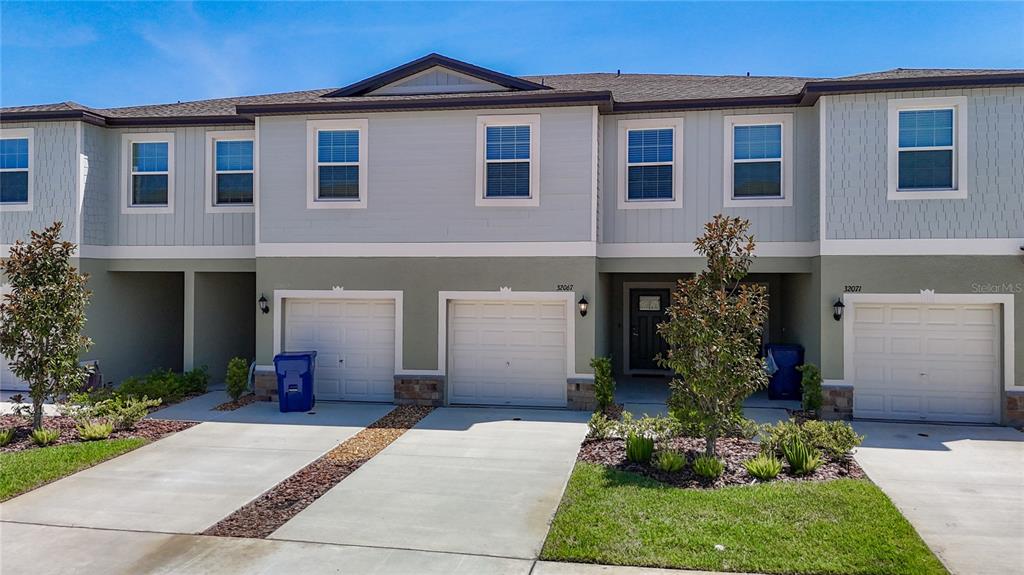 A multi-unit townhouse exterior features three garage doors, light-colored siding, and small front landscaping — 32067 SPICEBERRY STREET, SAN ANTONIO, FL
