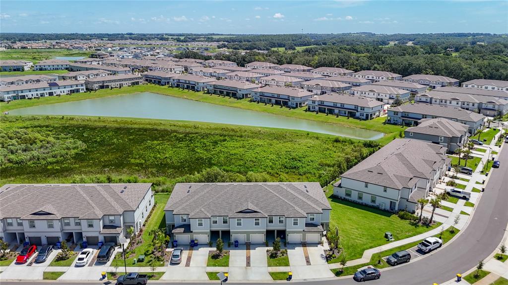 An aerial view shows multiple rows of townhomes surrounding a large retention pond — 32067 SPICEBERRY STREET, SAN ANTONIO, FL