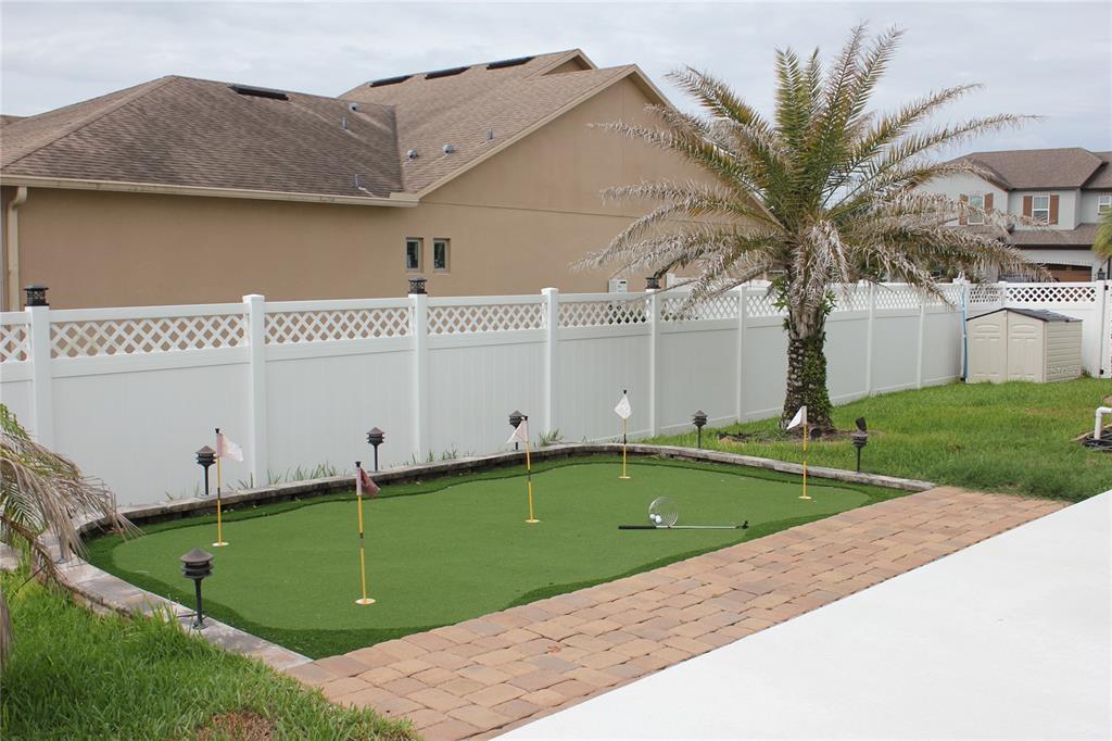 A backyard putting green with four flags and a paver patio next to a white fence — 4203 CAPLOCK STREET, CLERMONT, FL