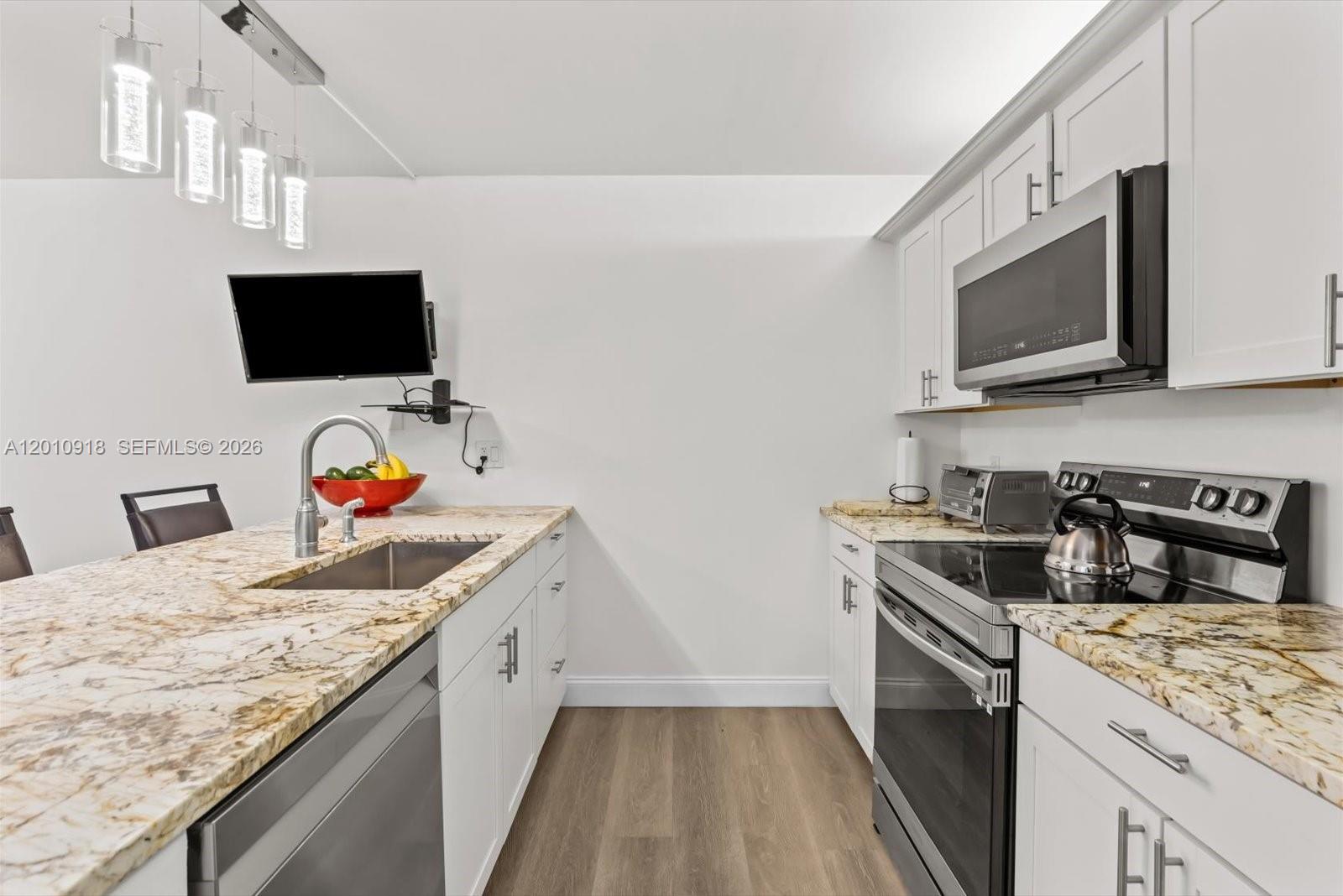 A modern kitchen features white cabinets, granite countertops, stainless steel appliances, and pendant lighting — 6001 60th Way, West Palm Beach FL 33409, WEST PALM BEACH, FL