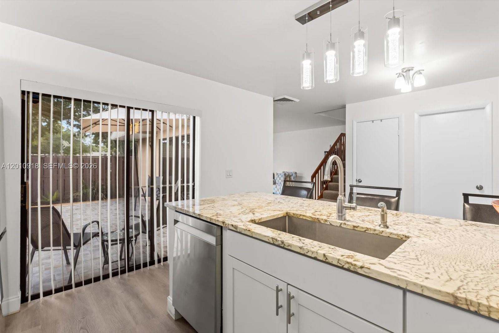 A kitchen island with a granite countertop and stainless steel sink faces a sliding glass door — 6001 60th Way, West Palm Beach FL 33409, WEST PALM BEACH, FL