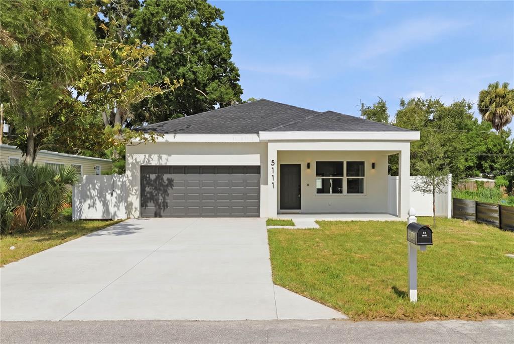 A single-story house with a gray garage door, white exterior, and a front porch — 5111 68TH STREET N, ST PETERSBURG, FL