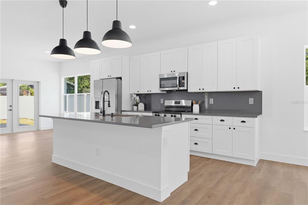 A modern kitchen features white cabinets, a gray island, and three black pendant lights — 5111 68TH STREET N, ST PETERSBURG, FL