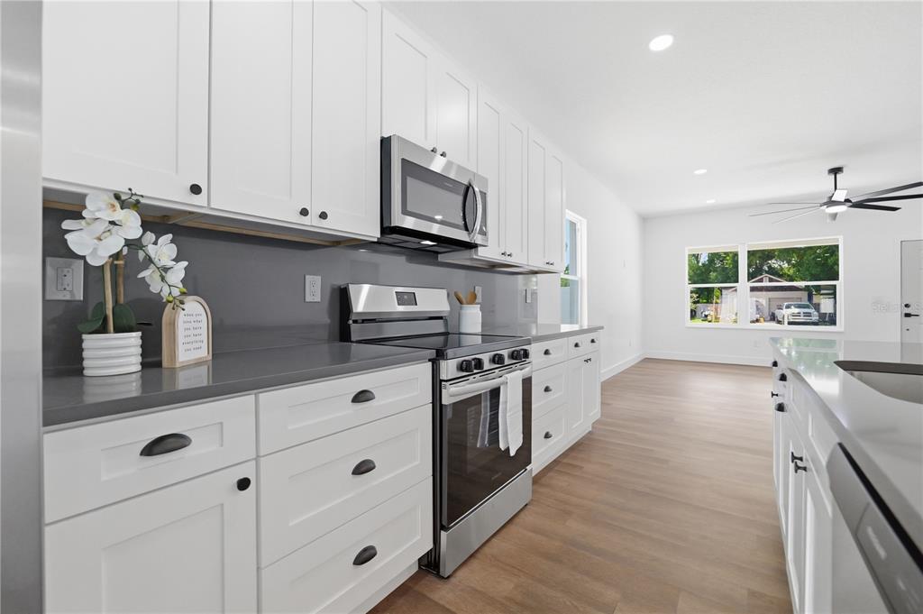 A modern kitchen features white shaker cabinets, gray countertops, and stainless steel appliances — 5111 68TH STREET N, ST PETERSBURG, FL