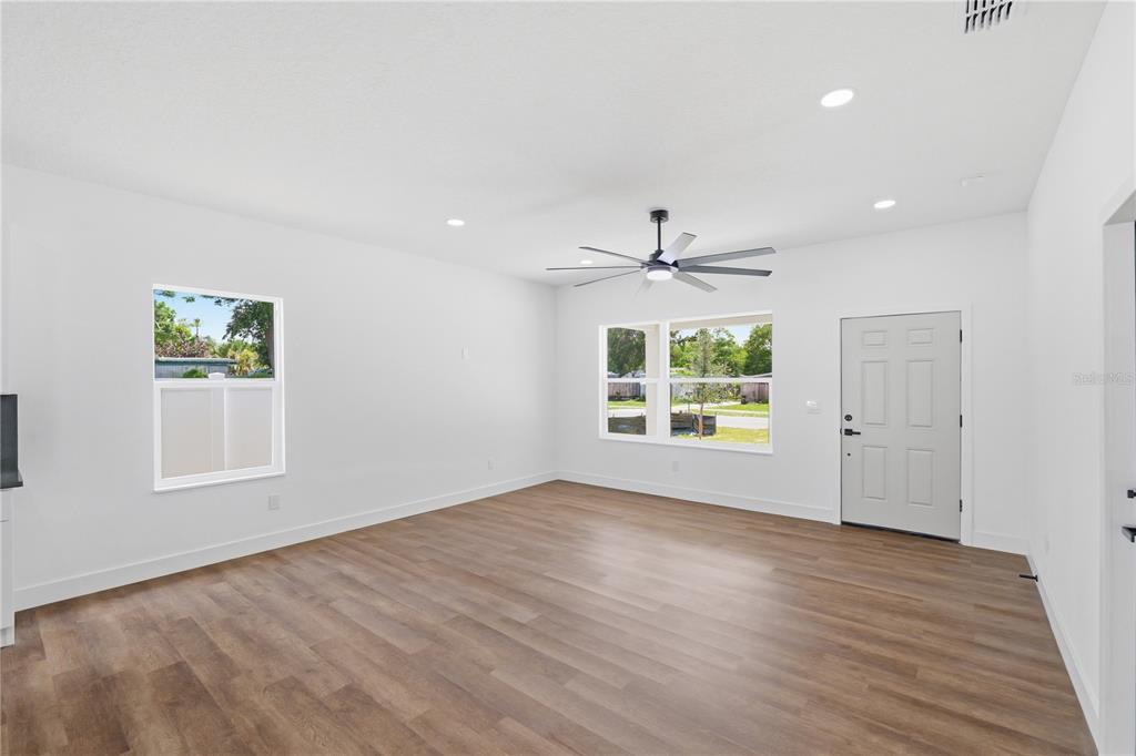 An empty living room features white walls, wood-look flooring, a ceiling fan, and exterior views — 5111 68TH STREET N, ST PETERSBURG, FL