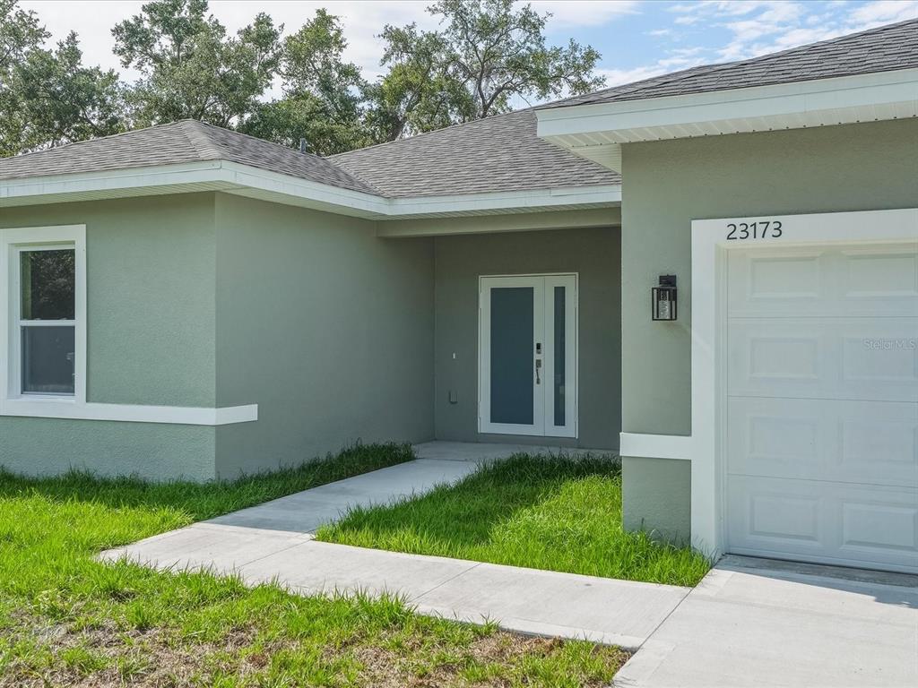 The exterior of a light green house features a white garage door and front door — 23173 GLEN AVENUE, PUNTA GORDA, FL
