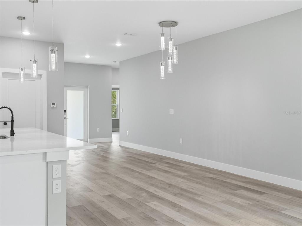 A modern kitchen and living area featuring light wood flooring, gray walls, and pendant lighting — 23173 GLEN AVENUE, PUNTA GORDA, FL