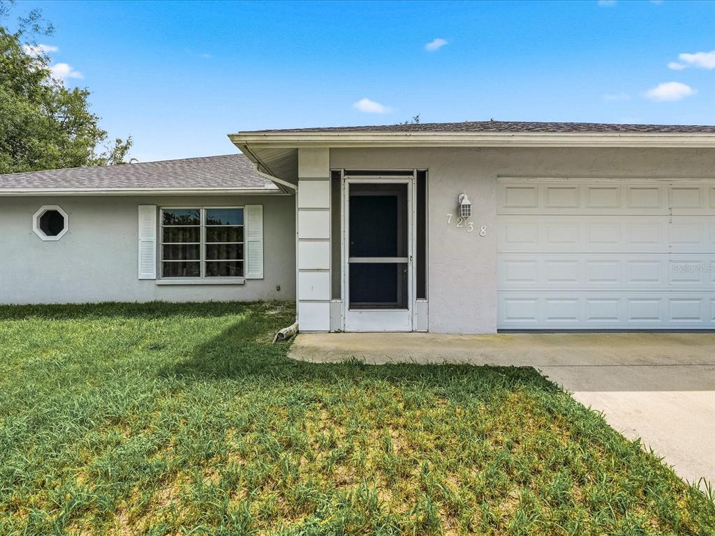 A single-story house exterior features a light gray stucco facade, a garage, and a front entrance — 7238 SPINNAKER BOULEVARD, ENGLEWOOD, FL