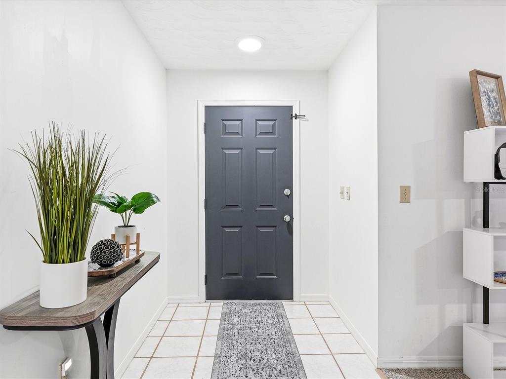 A bright entryway features a dark gray front door, white tiled floors, and a console table — 7238 SPINNAKER BOULEVARD, ENGLEWOOD, FL