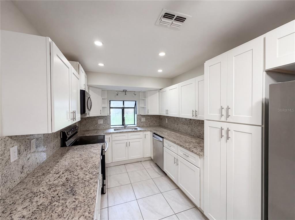 A kitchen features white cabinets, granite countertops, stainless steel appliances, and light tile flooring — 10510 SW 74TH COURT, OCALA, FL