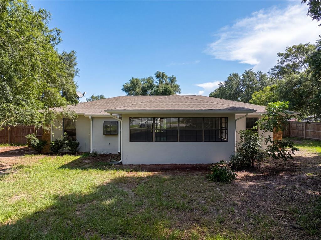 The exterior view of a single-story house features a large window, light-colored siding, and trees — 10510 SW 74TH COURT, OCALA, FL