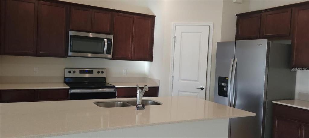 A kitchen features dark wood cabinets, stainless steel appliances, and a central island with sink — 2713 FRANKLIN ROAD, ST CLOUD, FL