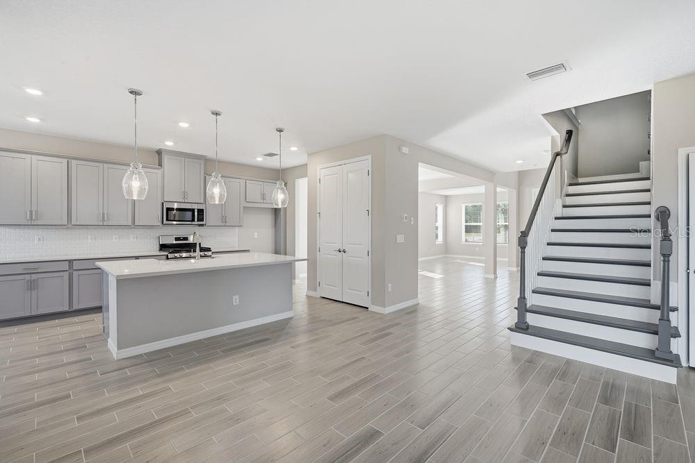 A kitchen with gray cabinets and a center island opens to a staircase and living area — 1678 TRAILHEAD LANE, ZEPHYRHILLS, FL
