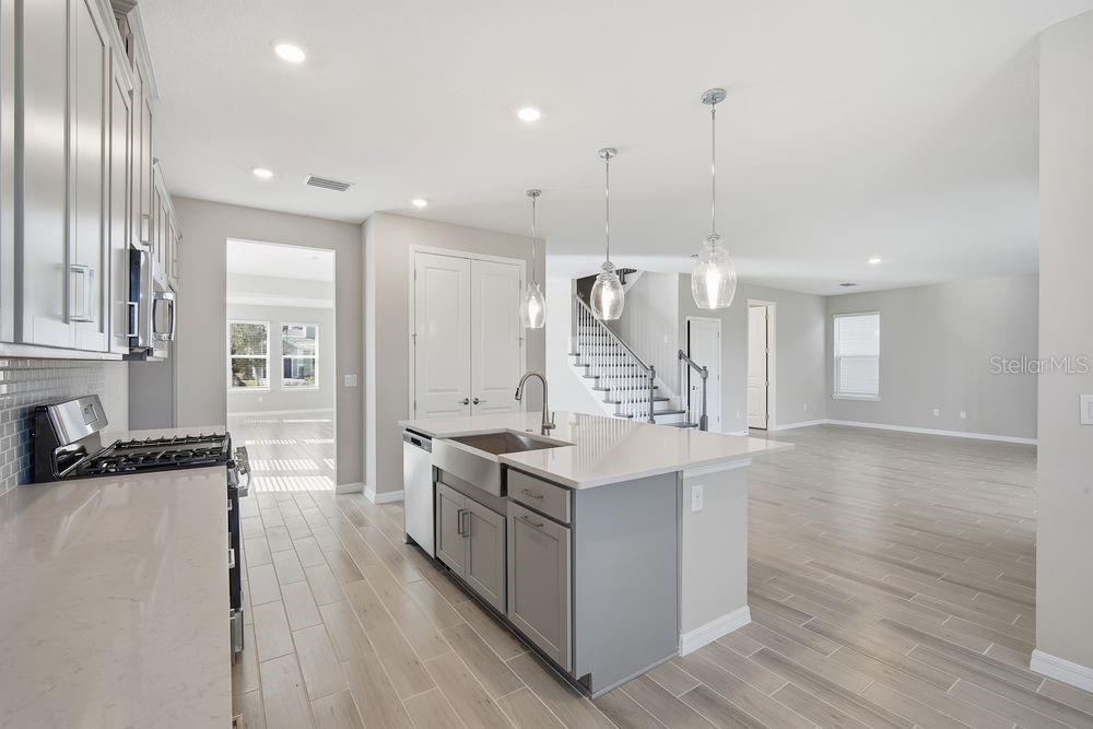 A modern kitchen with gray cabinets, a white quartz island, and light wood-look flooring — 1678 TRAILHEAD LANE, ZEPHYRHILLS, FL