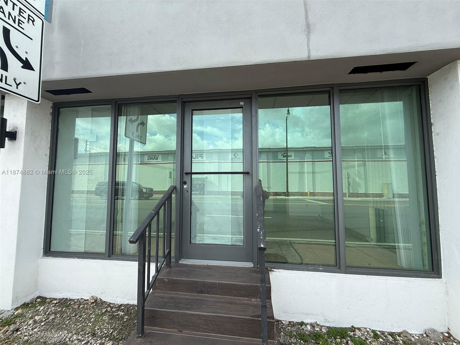 A glass-paneled entry door with a small staircase is set into a white exterior wall — 801 Monterey St # 101, Coral Gables FL 33134, CORAL GABLES, FL
