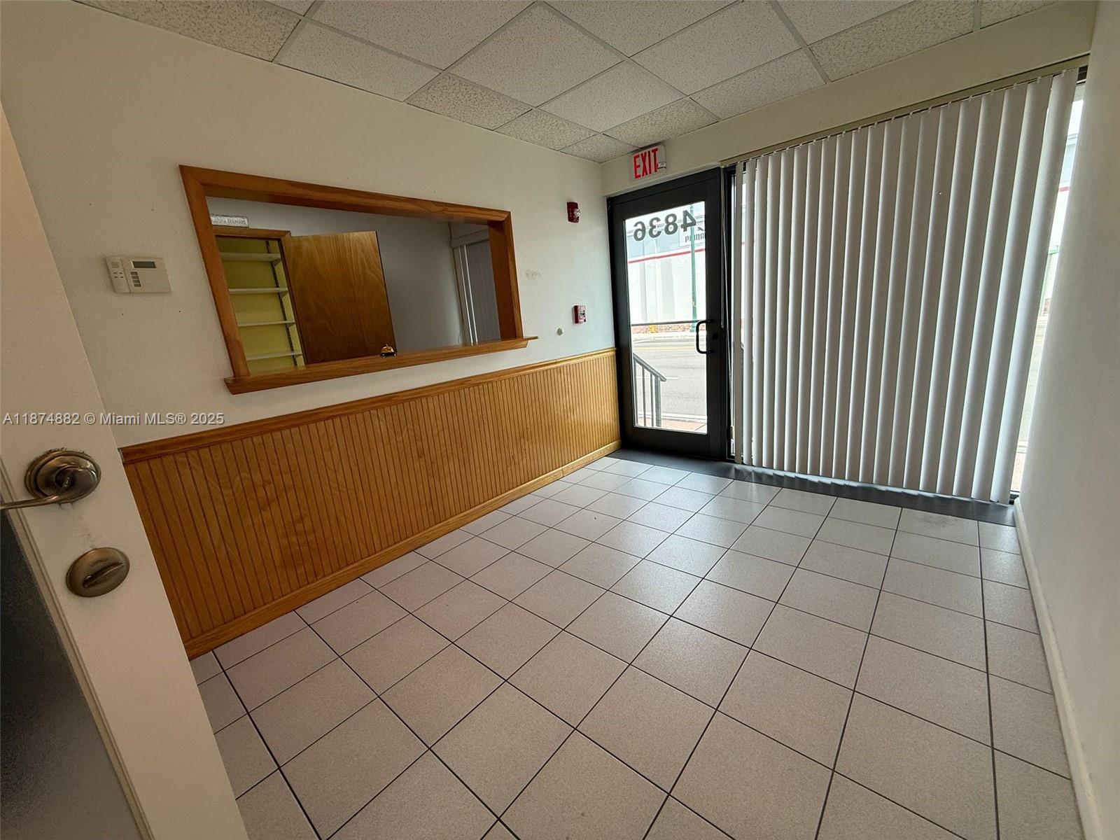 A small commercial space features white tiled floors, wood wainscoting, a service window, and vertical blinds — 801 Monterey St # 101, Coral Gables FL 33134, CORAL GABLES, FL
