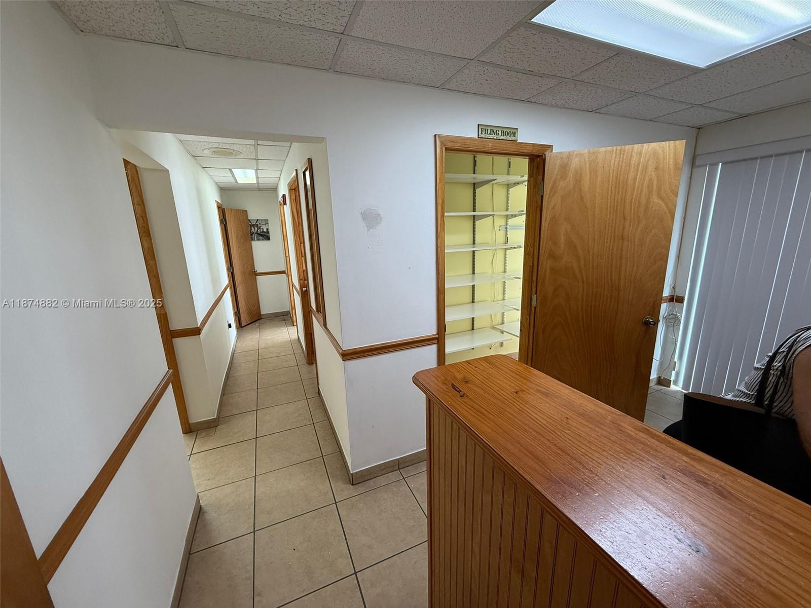 An office hallway features tiled floors, wooden trim, and a designated filing room with shelves — 801 Monterey St # 101, Coral Gables FL 33134, CORAL GABLES, FL