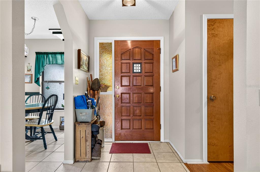 An entryway features a wood front door, tiled floor, and a view into a dining area — 7706 WILLOW BROOK COURT, HUDSON, FL