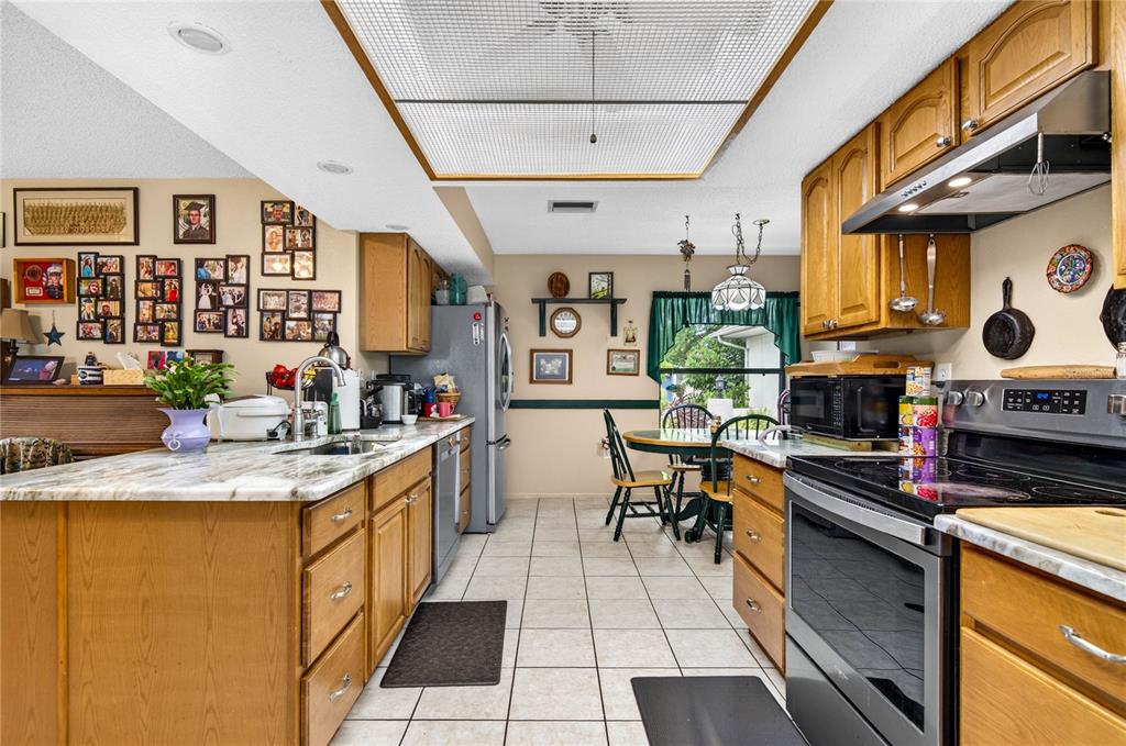 A kitchen features wood cabinets, a marble-look countertop, a tile floor, and a grid ceiling — 7706 WILLOW BROOK COURT, HUDSON, FL