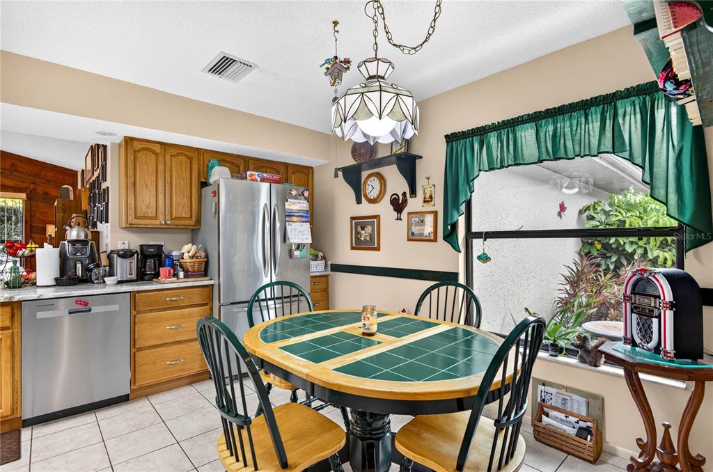A kitchen with wood cabinets, a tile-topped dining table, and a window with green curtains — 7706 WILLOW BROOK COURT, HUDSON, FL