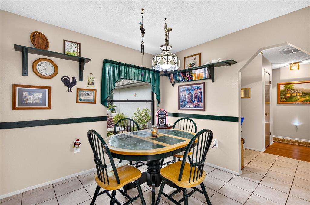 A dining area features a tile-topped table, wooden chairs, wall shelves, and a hanging lamp — 7706 WILLOW BROOK COURT, HUDSON, FL
