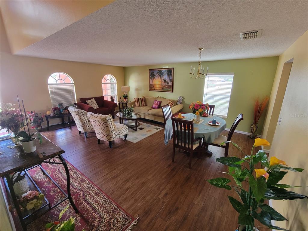 An open-concept living and dining area features wood-look flooring, light green walls, and arched windows — 2242 WOOD COURT, DELTONA, FL