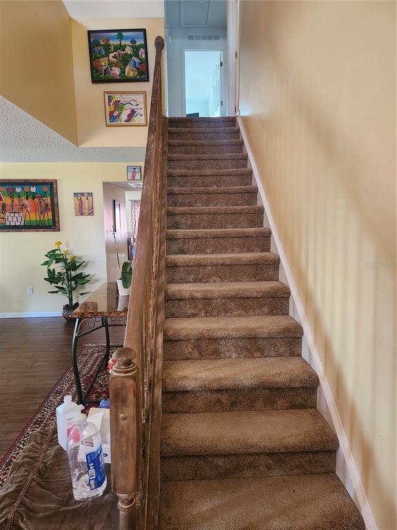 A carpeted staircase with a wooden railing leads to an upper level in a home — 2242 WOOD COURT, DELTONA, FL