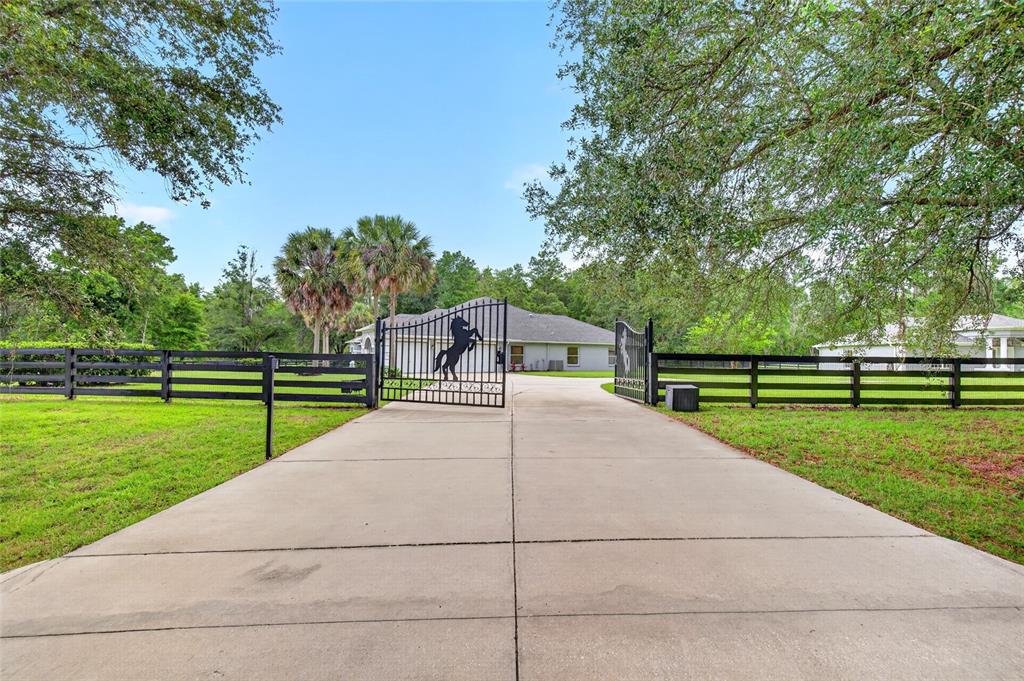 A concrete driveway leads to a gated entrance with a horse silhouette in front of a house — 14144 NW 141ST AVENUE, WILLISTON, FL
