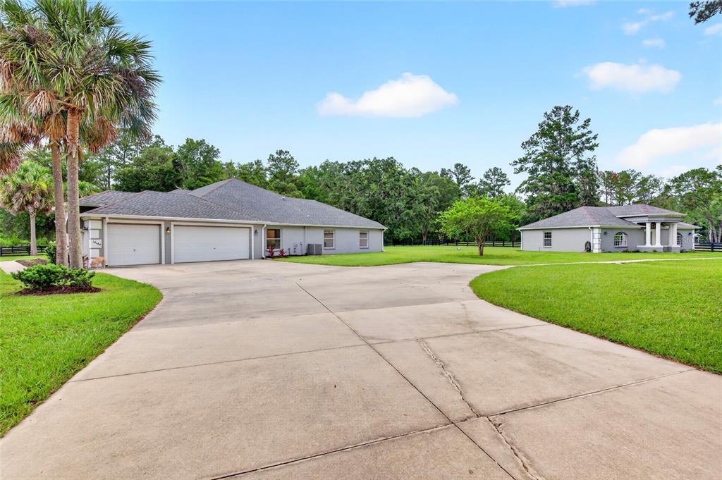 A concrete driveway leads to a large house with a three-car garage and detached structure — 14144 NW 141ST AVENUE, WILLISTON, FL
