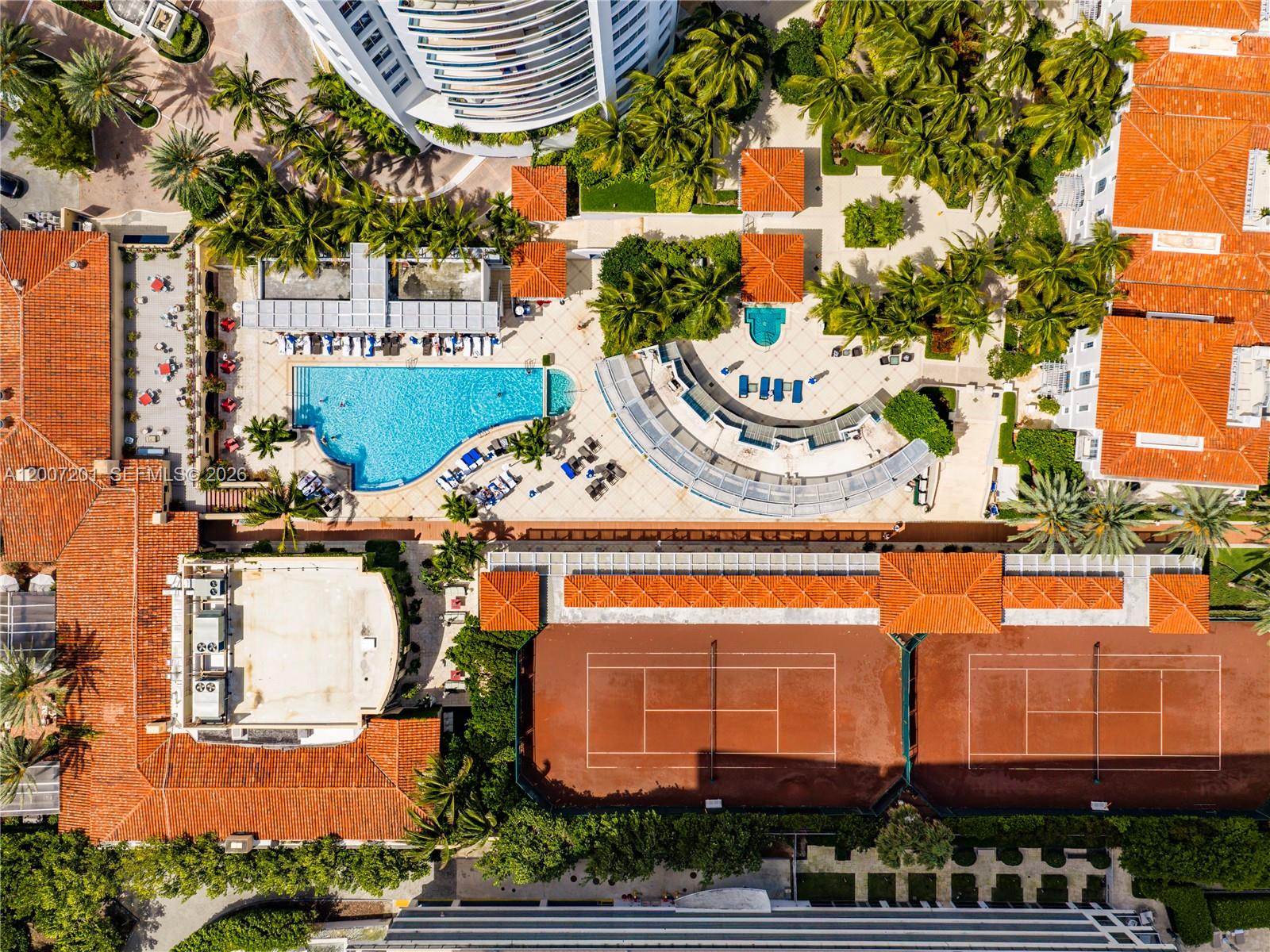 An aerial view shows a swimming pool, tennis courts, and surrounding buildings with orange roofs — 5959 Collins Ave # 906, Miami Beach FL 33140, MIAMI BEACH, FL