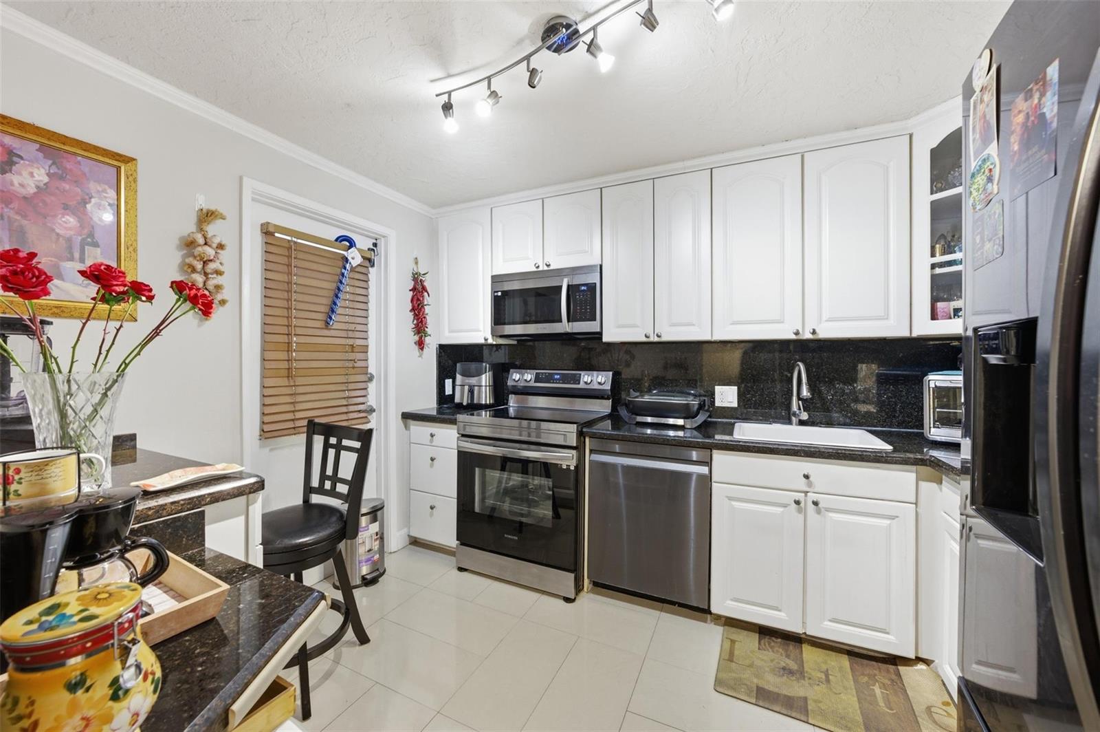 A kitchen features white cabinets, black granite countertops, stainless steel appliances, and tile flooring — 3000 S Course Drive # 201, Pompano Beach FL 33069, POMPANO BEACH, FL
