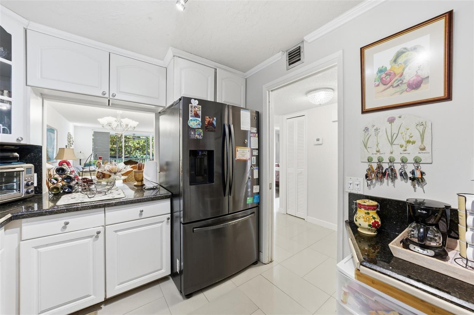 A kitchen features white cabinets, black granite countertops, a stainless steel refrigerator, and tiled floors — 3000 S Course Drive # 201, Pompano Beach FL 33069, POMPANO BEACH, FL