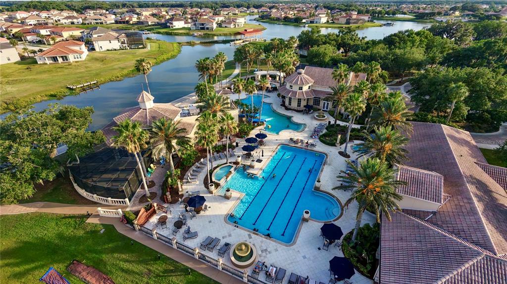 An aerial view shows a community swimming pool complex surrounded by palm trees and houses — 3311 BENT PADDLE DRIVE, KISSIMMEE, FL