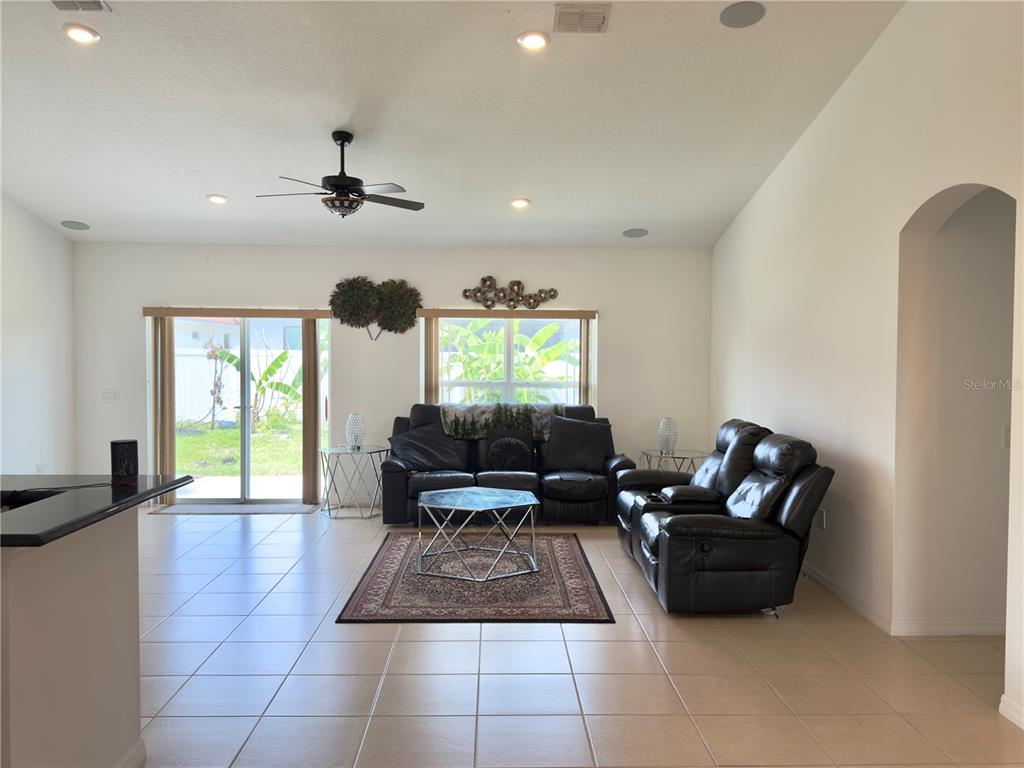 A living room features tile flooring, a ceiling fan, leather furniture, and sliding glass doors — 3311 BENT PADDLE DRIVE, KISSIMMEE, FL