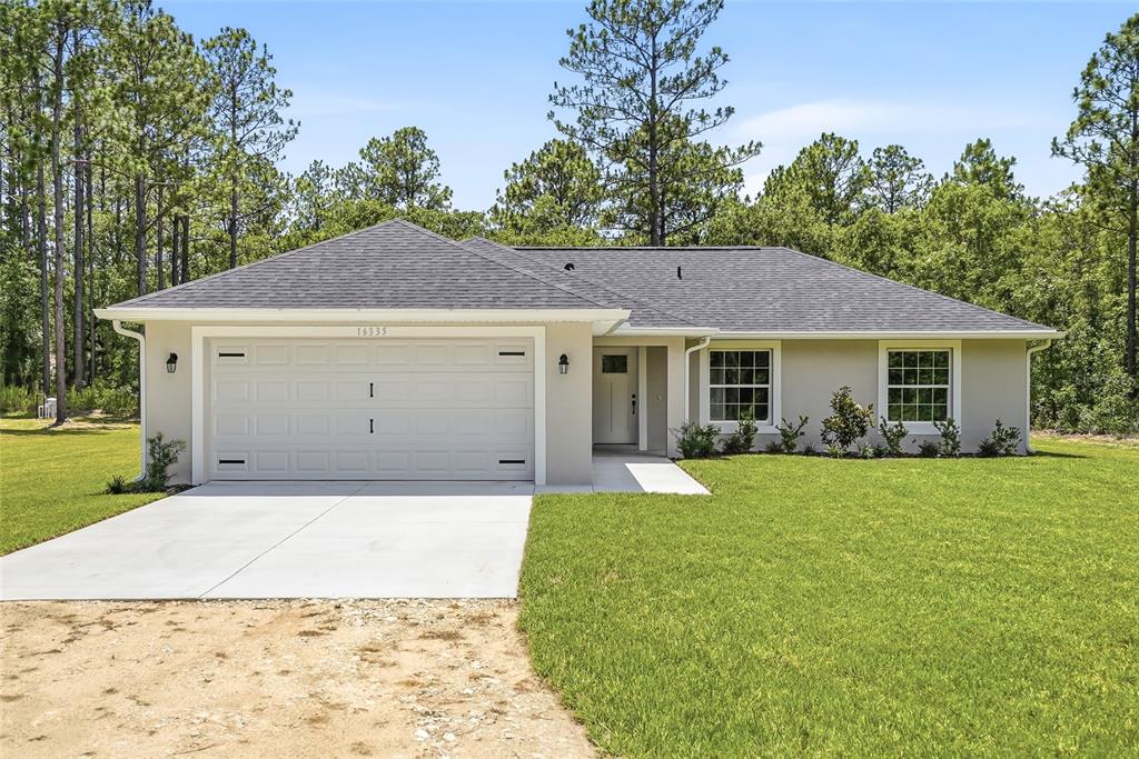 A single-story house with a two-car garage, light-colored stucco exterior, and a dark shingled roof — 16335 FORCE ROAD, WEEKI WACHEE, FL
