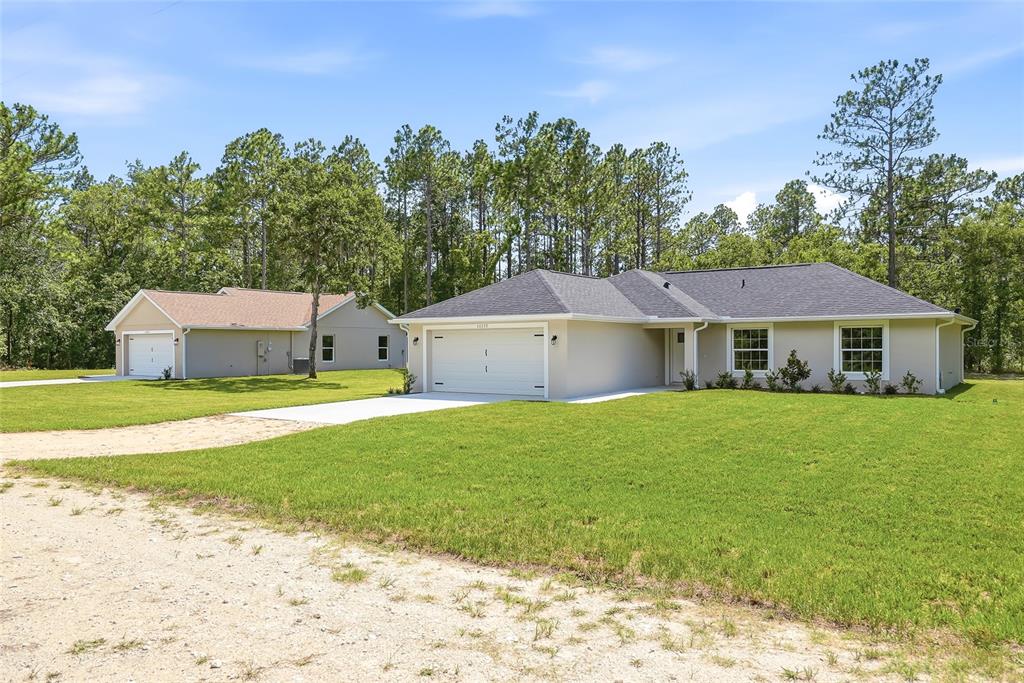 Two single-story houses with garages sit on a grassy lot bordered by a forest — 16335 FORCE ROAD, WEEKI WACHEE, FL