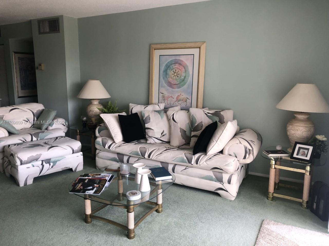 A living room features a floral sofa, matching armchair, glass coffee table, and two lamps — 1000 NE 14th Ave # 605, Hallandale Beach FL 33009, HALLANDALE BEACH, FL