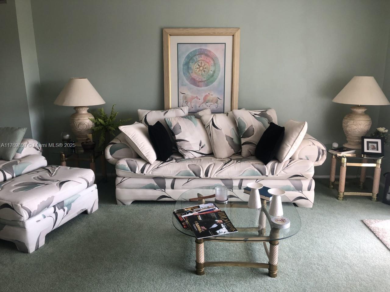 A living room features a patterned sofa, matching armchair, glass coffee table, and two table lamps — 1000 NE 14th Ave # 605, Hallandale Beach FL 33009, HALLANDALE BEACH, FL