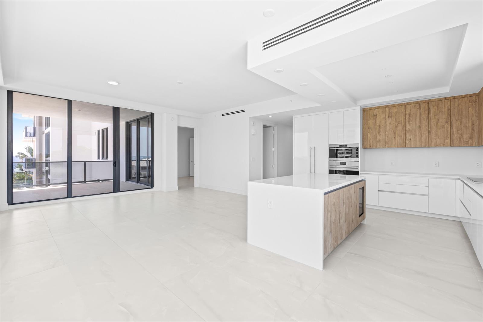 A modern kitchen and living area featuring white cabinetry, wood accents, and a large island — 305 Briny Avenue # 406, Pompano Beach FL 33062, POMPANO BEACH, FL