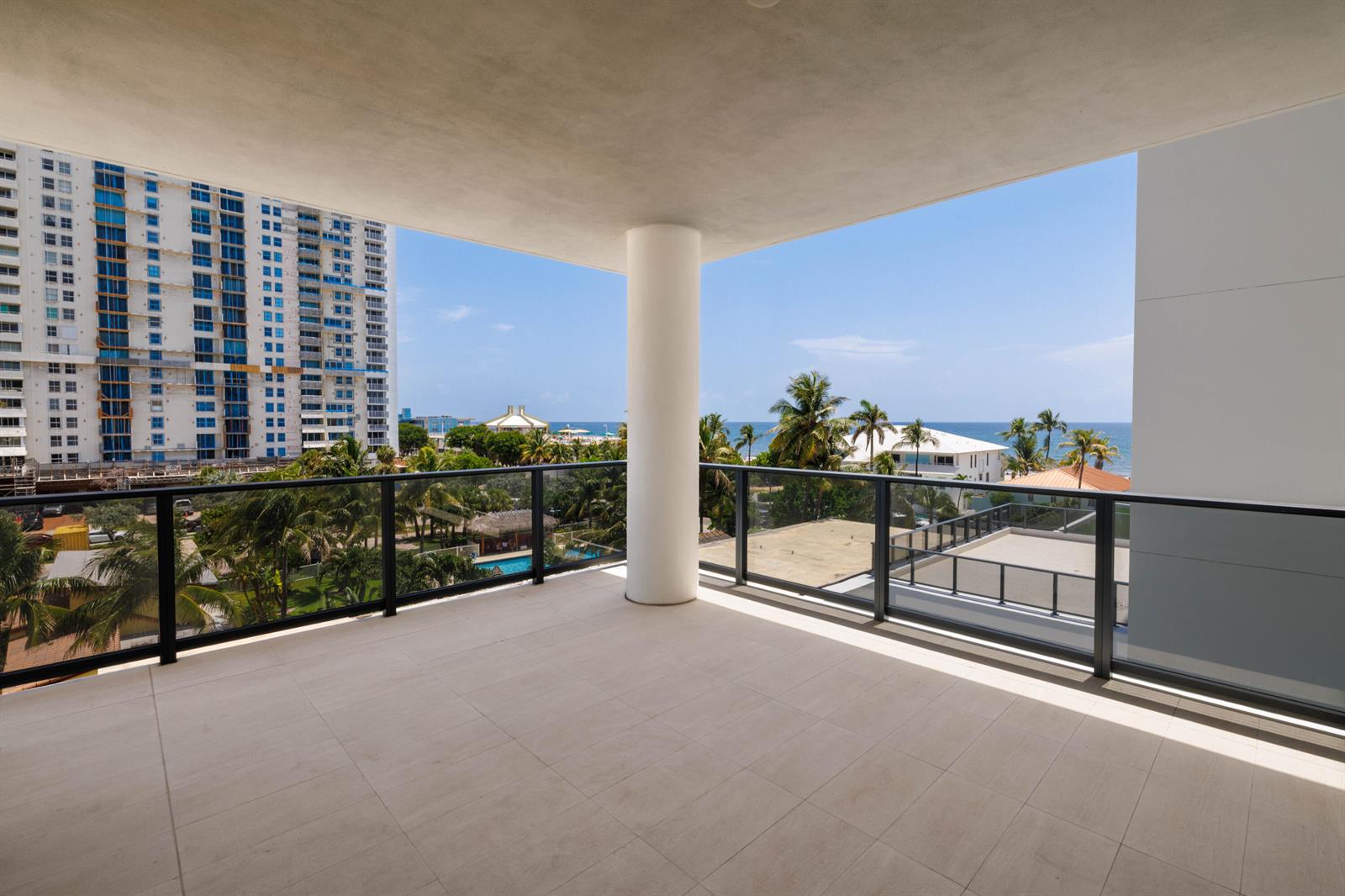 A spacious, tiled balcony features a central support column and glass railings overlooking the ocean — 305 Briny Avenue # 406, Pompano Beach FL 33062, POMPANO BEACH, FL