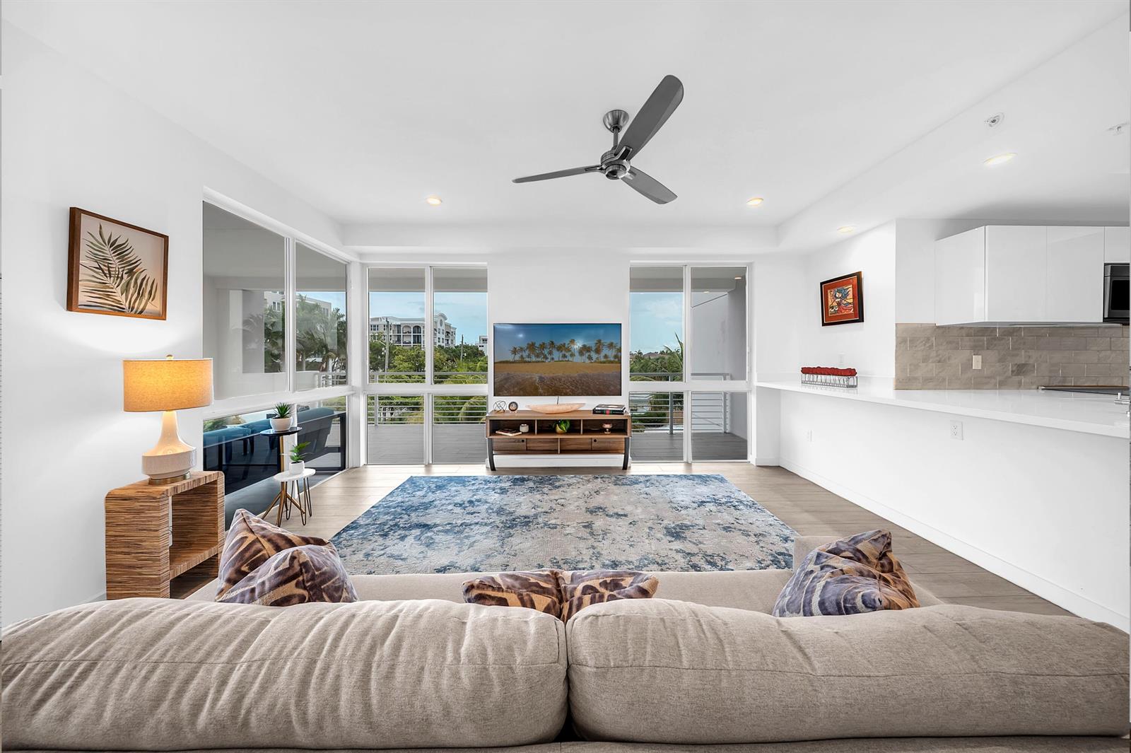 A bright living room features a large area rug, a television console, and floor-to-ceiling windows — 51 SE 19th Avenue # 303, Deerfield Beach FL 33441, DEERFIELD BEACH, FL