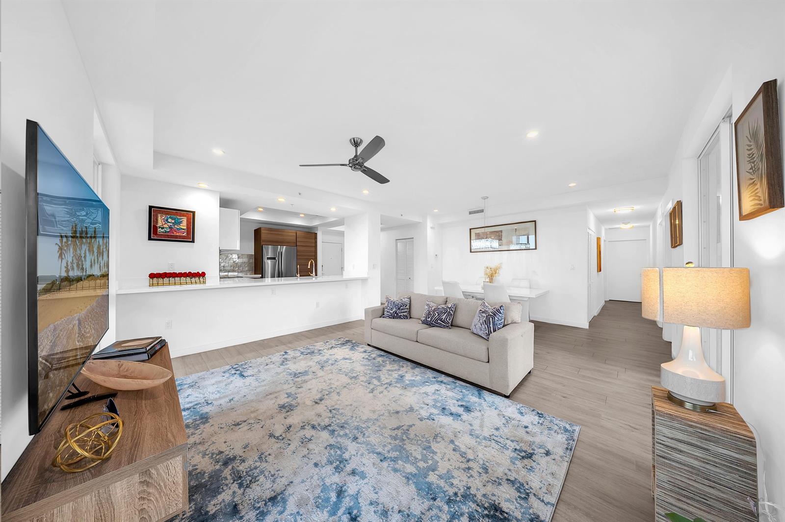 A modern living room features a grey sofa, a blue patterned rug, and an open kitchen — 51 SE 19th Avenue # 303, Deerfield Beach FL 33441, DEERFIELD BEACH, FL