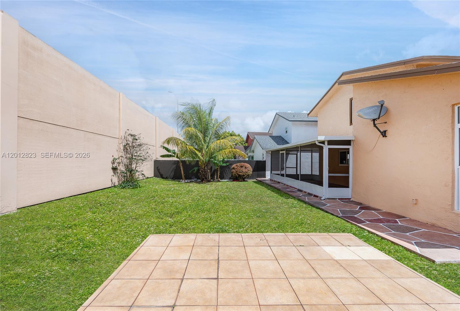 A backyard features a tiled patio, a screened-in porch, and a grassy lawn — 1007 NW 106th Ave Cir, Miami FL 33172, MIAMI, FL