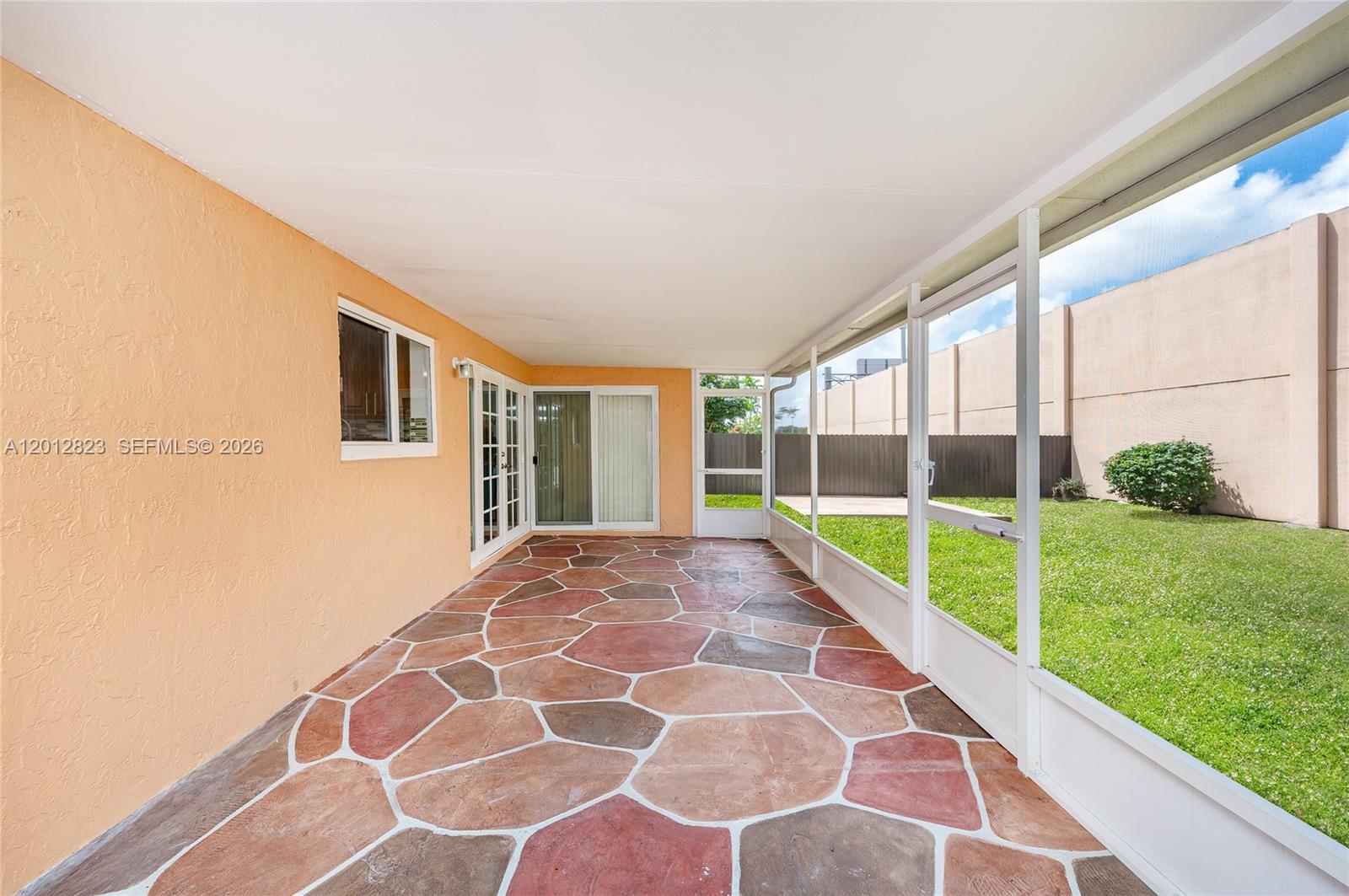 A covered patio features a flagstone-patterned floor, peach-colored walls, and a screened-in wall — 1007 NW 106th Ave Cir, Miami FL 33172, MIAMI, FL
