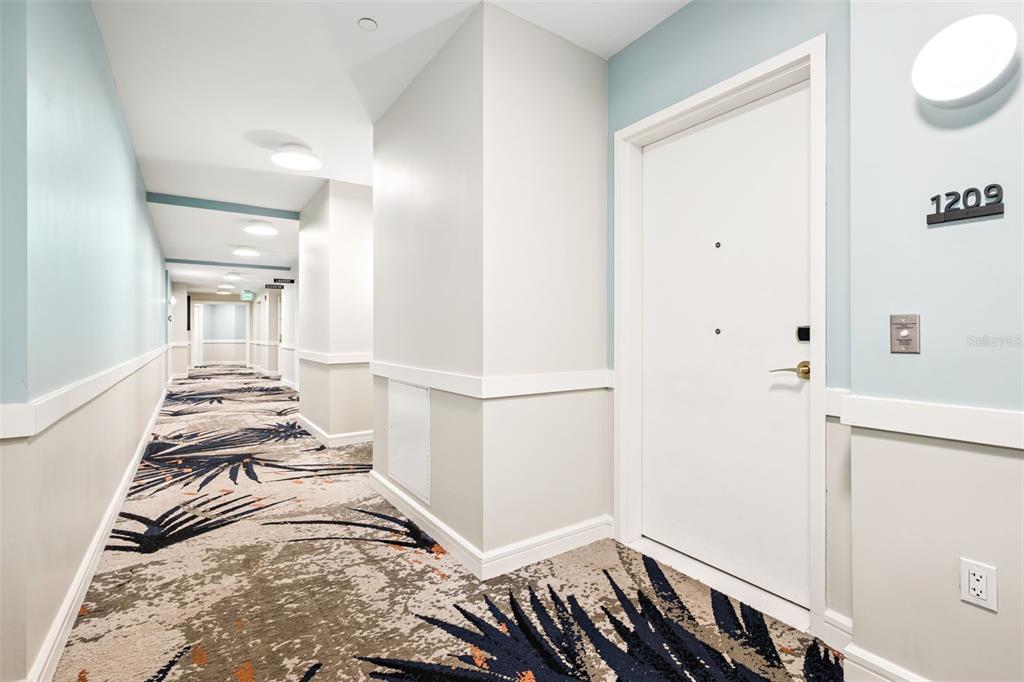 A hallway with patterned carpet leads to a white door labeled 1209 — 3151 SUNSET WALK DRIVE UNIT 1209, KISSIMMEE, FL