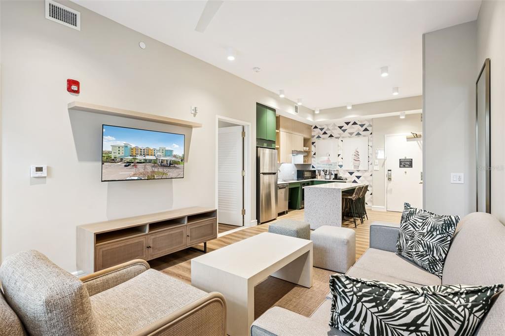 A modern living room features a wall-mounted television, light wood furniture, and an open kitchen — 3151 SUNSET WALK DRIVE UNIT 1209, KISSIMMEE, FL