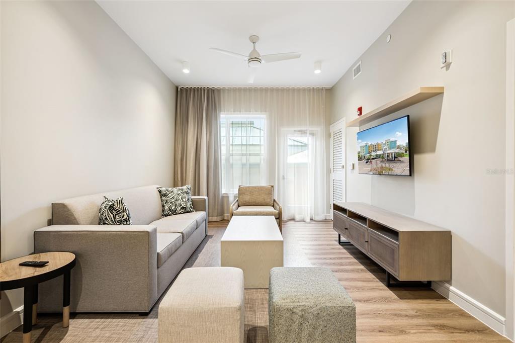 A living room featuring a gray sofa, a coffee table, two ottomans, and a wall-mounted television — 3151 SUNSET WALK DRIVE UNIT 1209, KISSIMMEE, FL