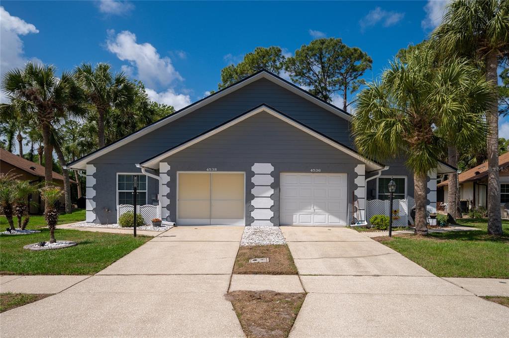 A duplex with gray siding, white trim, two garage doors, and palm trees in front — 4538 ROCKLEDGE LANE, PORT ORANGE, FL